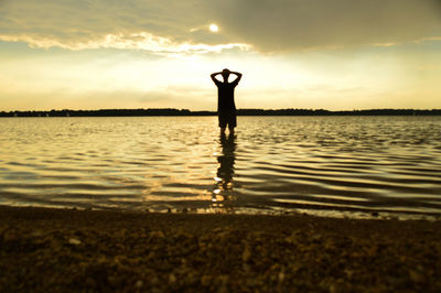 Silhouette man standing by lake against sky during sunset