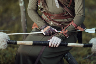 Midsection of archer holding bow and arrow against blurred background