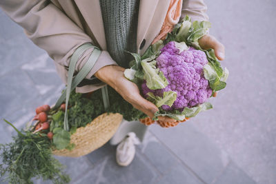 Hands of woman holding purple cauliflower and bags of vegetables on footpath