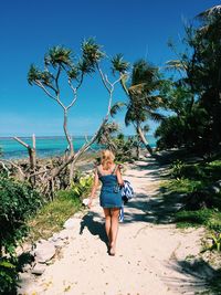 Rear view of woman walking on beach against sky