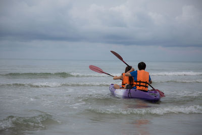 Rear view of friends sailing in boat on sea against cloudy sky