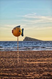 Toy on beach by sea against sky during sunset