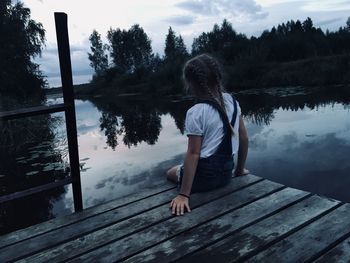 Full length of woman sitting on pier over lake against sky