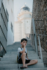 Boy sitting on staircase against building