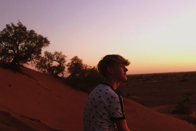 Side view of woman looking away against sky during sunset