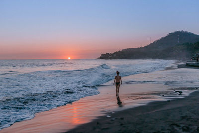 Man on beach against clear sky during sunset