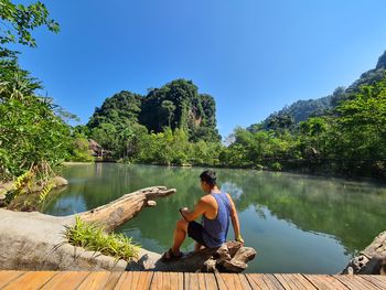 Man sitting by lake against sky