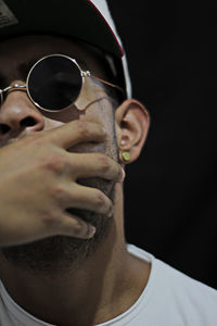 Close-up of man wearing sunglasses and cap against black background