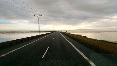 Road by sea against sky during sunset