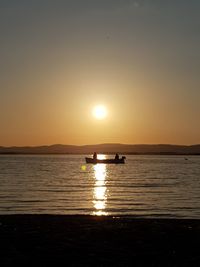 Silhouette people on boat in sea against clear sky during sunset