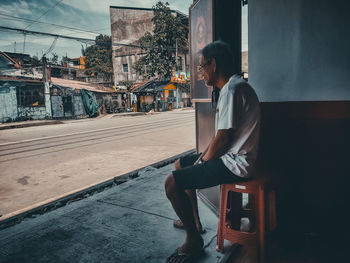 Side view of young woman sitting against buildings in city