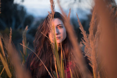 Thoughtful young woman looking away while standing amidst plants during sunset