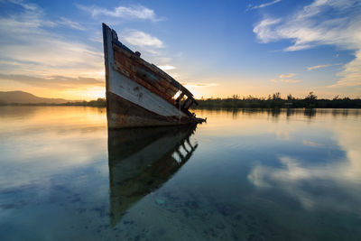 Boat moored in lake against sky during sunset