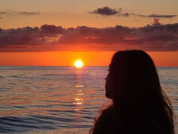 Silhouette woman looking at sea against sky during sunset