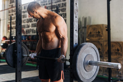 Shirtless man lifting barbell in gym