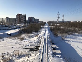 Snow covered railroad tracks in city against sky