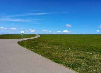 Road amidst field against blue sky