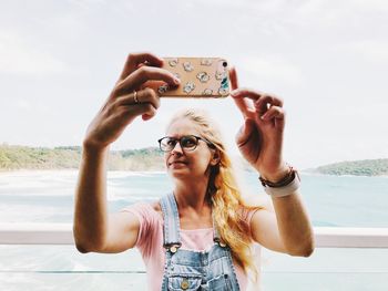 Woman photographing with mobile phone against sea and sky