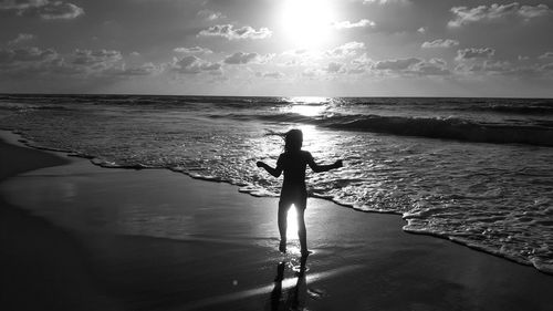 Silhouette woman standing on beach against sky during sunset