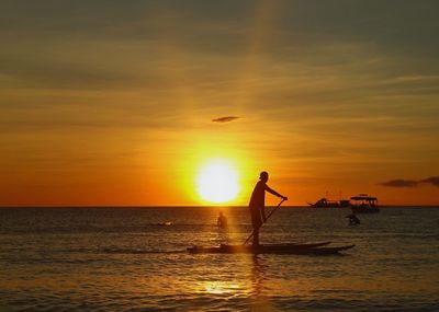 Silhouette people standing on sea against sky during sunset