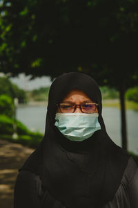 Young muslim woman wearing glasses and hijab head scarf and face mask at the outdoor park.