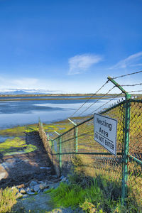 Information sign on riverbank against sky