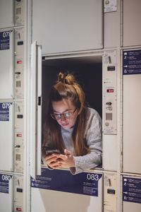 Young woman using phone in locker