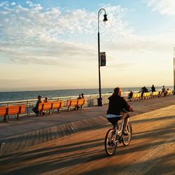 People on bicycle by sea against sky