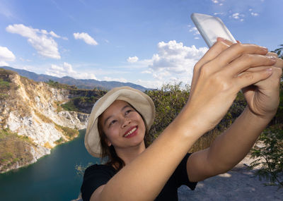 Portrait of smiling young woman against mountains in sky