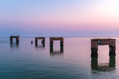 Wooden posts in sea against sky during sunset