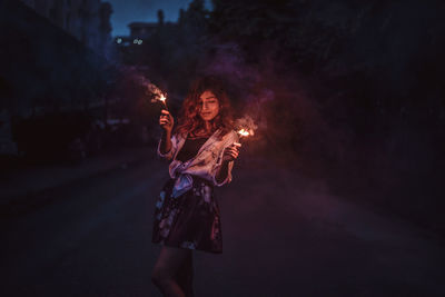 Woman standing by illuminated fire at night