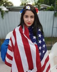 Portrait of beautiful young woman covered with american flag in back yard