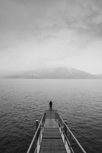 Rear view of man standing on jetty over lake against sky