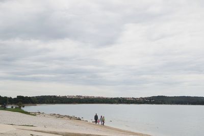 Family walking at beach against cloudy sky