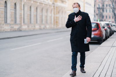 Full length of man wearing mask walking on sidewalk in city