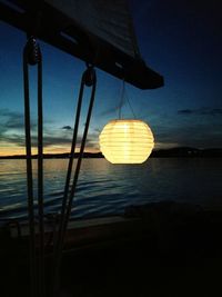 Illuminated light bulbs hanging from sea at sunset