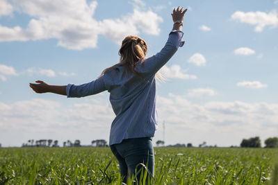 Rear view of woman with arms raised standing on field