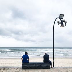 Man sitting on beach against sky