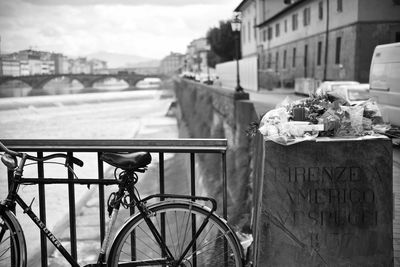 Bicycle on railing by river in city against sky