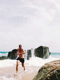 Full length of man enjoying by rock at beach against sky