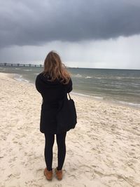 Rear view of woman standing on beach against sky