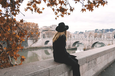 Rear view of woman sitting on retaining wall against sky