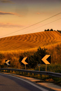 Road by field against sky during sunset