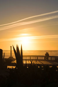 Silhouette people by sea against sky during sunset