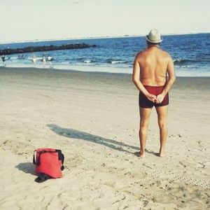 Rear view of shirtless man walking on beach