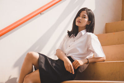 Portrait of young woman sitting on staircase against wall