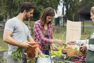 Mid adult couple selling garden vegetable to female customer