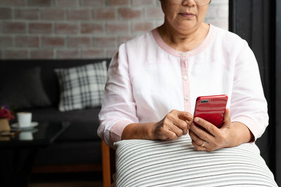 Senior woman using mobile phone while sitting on sofa at home