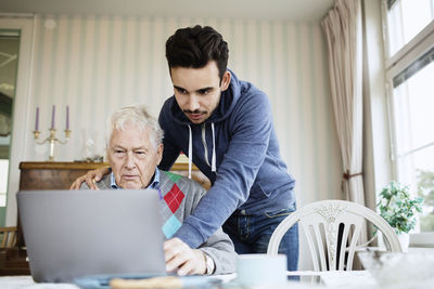 Caretaker assisting senior male in using laptop at nursing home