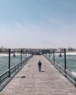 Rear view of man on pier over river against sky